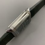 Flat lay of the steel JLC Reverso replica with its green leather strap laid open on a dark surface