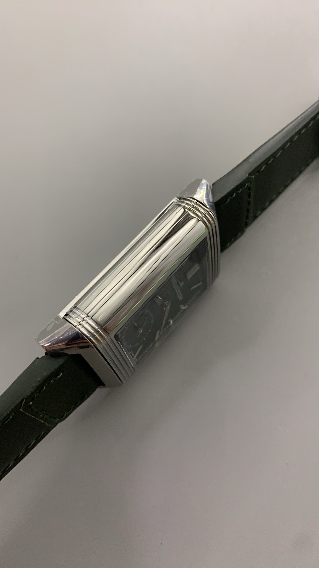 Flat lay of the steel JLC Reverso replica with its green leather strap laid open on a dark surface