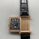 Full view of the rose gold Reverso replica with the black alligator strap coiled behind it