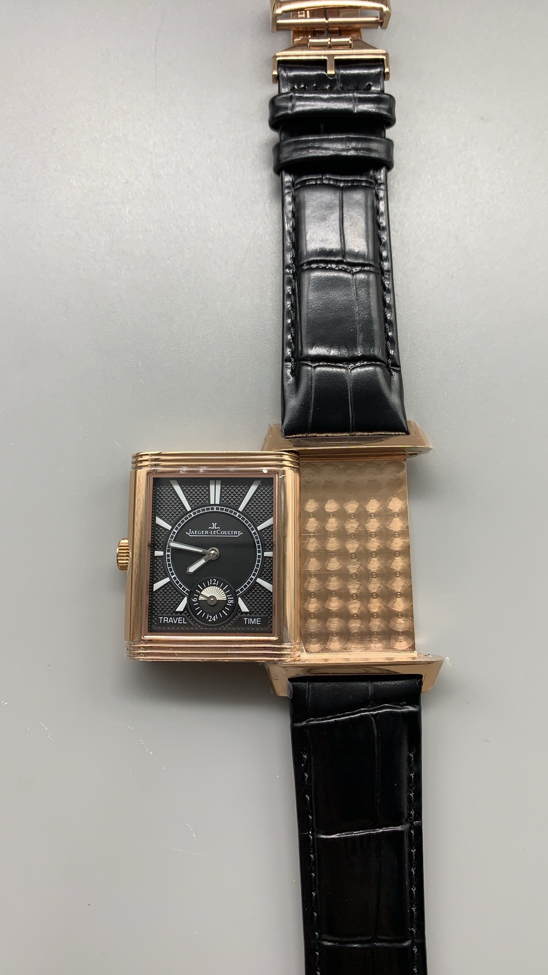 Full view of the rose gold Reverso replica with the black alligator strap coiled behind it